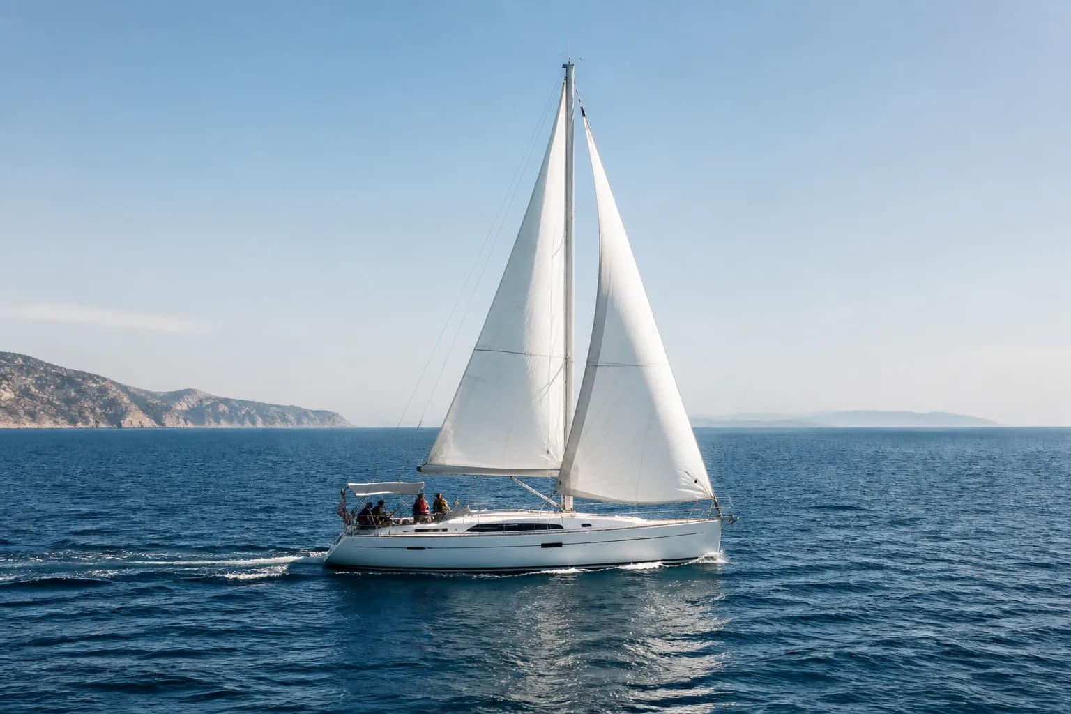 Illustrative cruising yacht under sail on open blue water with distant headlands.